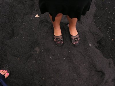 a photo of sandaled feet on black sand beach