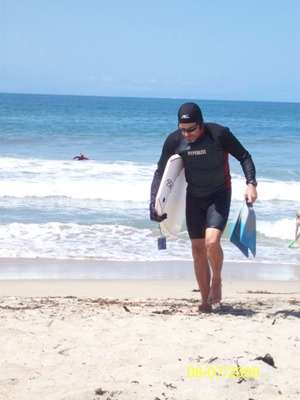 man with boogie board in wetsuit walking up the beach