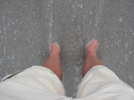 photo of man's feet in sand at shoreline